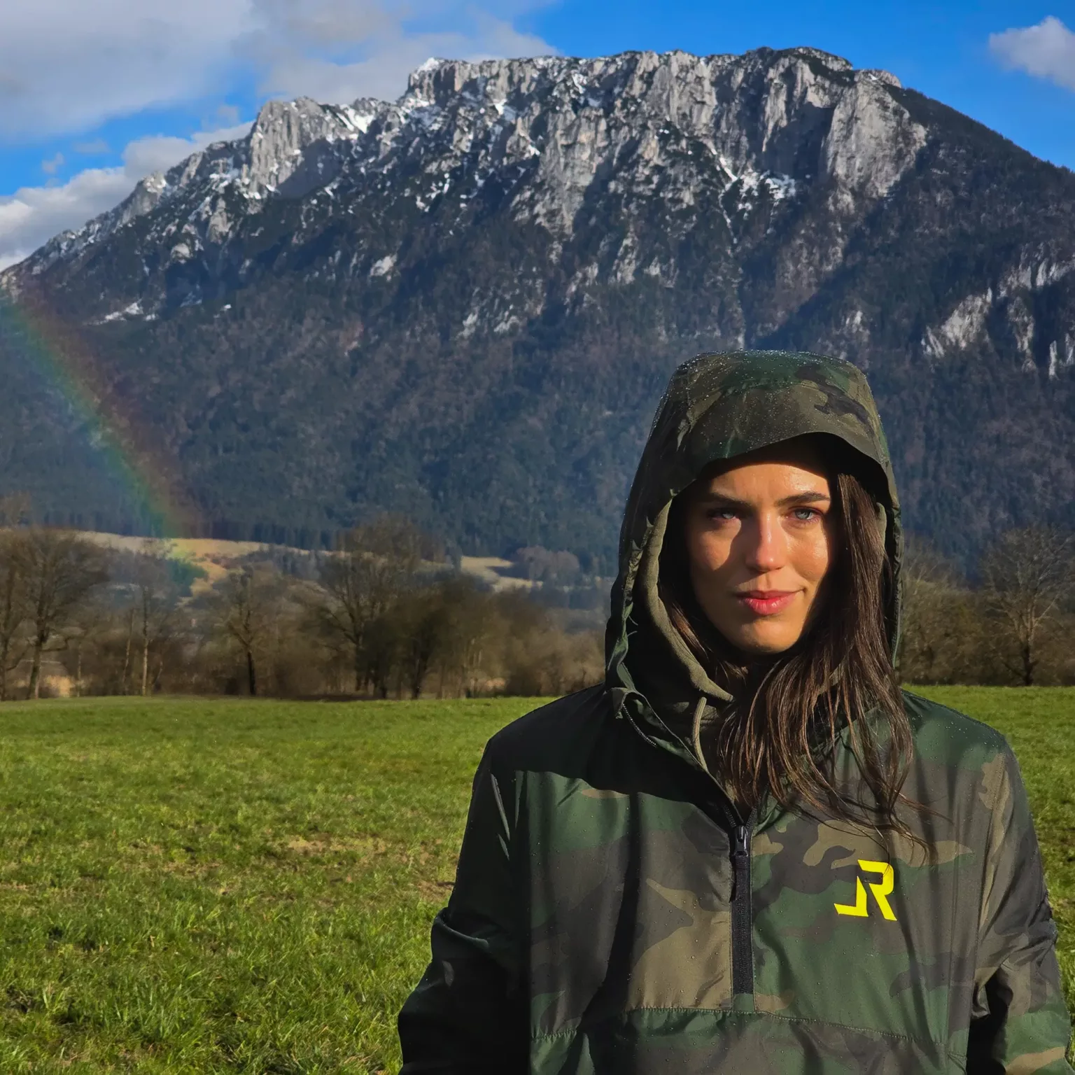 LavendersRanch Windbreaker Jacket camouflage – woman wearing camo jacket with hood up in front of mountain in the rain with a rainbow.