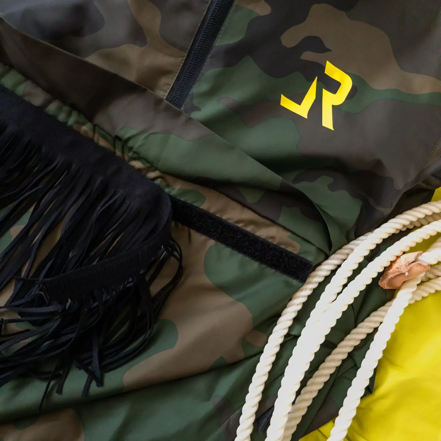 LavendersRanch Tazzel Fringe in citrus and black on windbreaker jackets – close-up of camouflage LavendersRanch windbreaker with detachable black suede fringe tazzel system and coiled rope