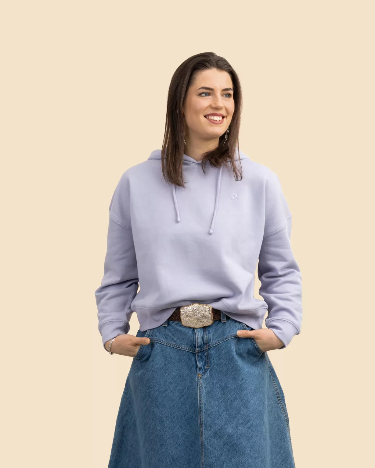 Woman wearing a lavender cropped hoodie by LavendersRanch (LR) with a tonal embroidered LR logo on the chest, styled with denim skirt, showcasing sustainable western country fashion.